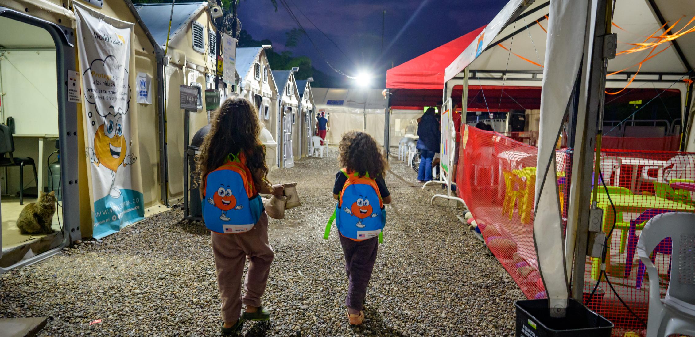©World Vision International/Rainhartd Two children staying at the CAS Hermanos Caminantes in March 2023 shelter head toward a tent for dinner. CAS Hermanos Caminantes is a shelter installed and managed by World Vision that is on the road that connects Cúcuta with Bucaramanga at the height of the municipality of Bochalema. 